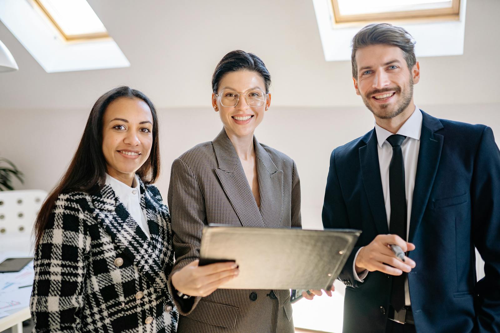 Office team of three professionals reviewing a tablet, looking at the camera