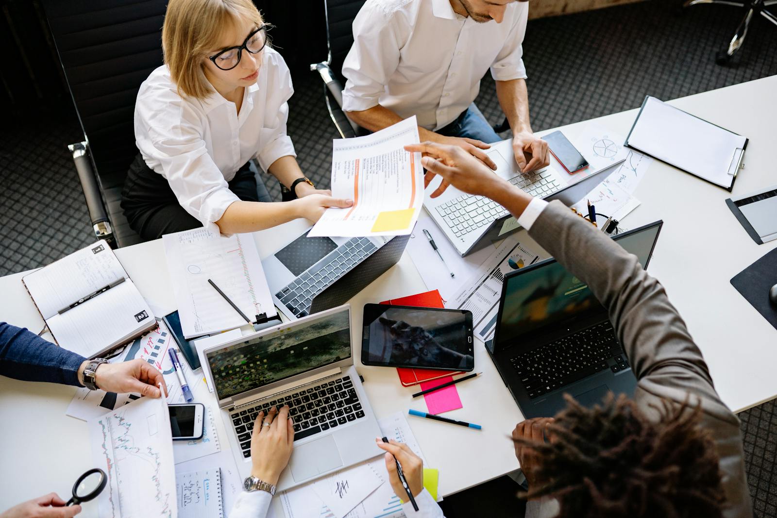 Colleagues collaborating around a table with laptops and documents, top-down view